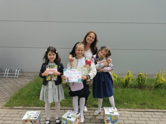 Uśmiechnięte dziewczynki trzymają dyplom oraz nagrody książki i globus za zajęcie 1 miejsca w Wojewódzkim Konkursie Ekologicznym. Za nimi stoi dumna pani. 