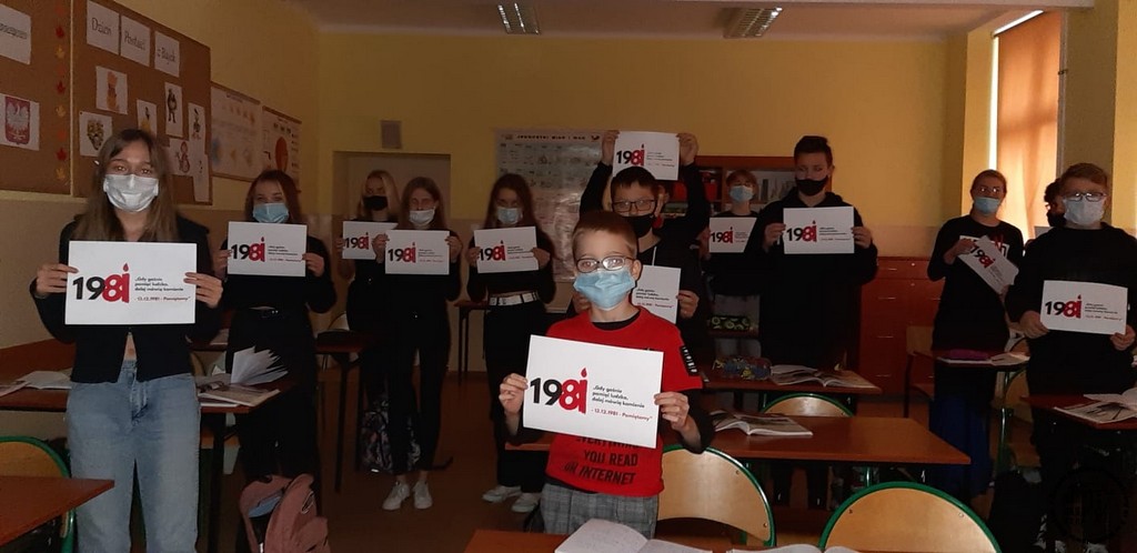 Uczniowie ubrani na czarno trzymają kartki z logo akcji "Gdy gaśnie pamięć ludzka, dalej mówią kamienie