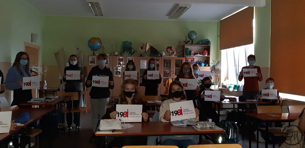 Uczniowie ubrani na czarno trzymają kartki z logo akcji "Gdy gaśnie pamięć ludzka, dalej mówią kamienie