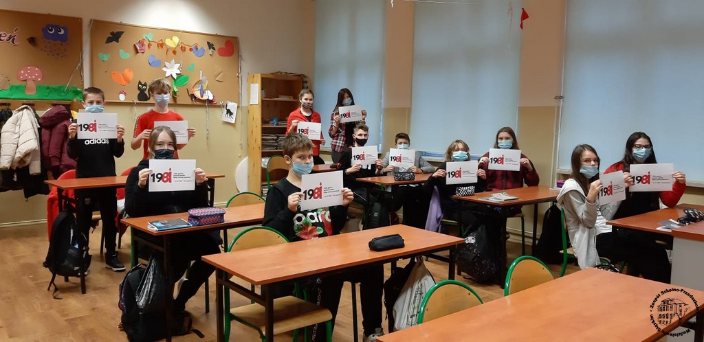 Uczniowie ubrani na czarno trzymają kartki z logo akcji "Gdy gaśnie pamięć ludzka, dalej mówią kamienie