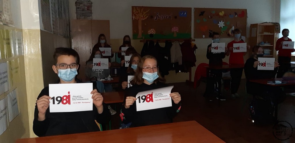 Uczniowie ubrani na czarno trzymają kartki z logo akcji "Gdy gaśnie pamięć ludzka, dalej mówią kamienie