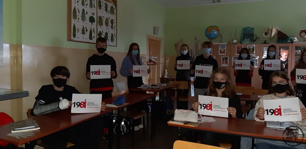 Uczniowie ubrani na czarno trzymają kartki z logo akcji "Gdy gaśnie pamięć ludzka, dalej mówią kamienie