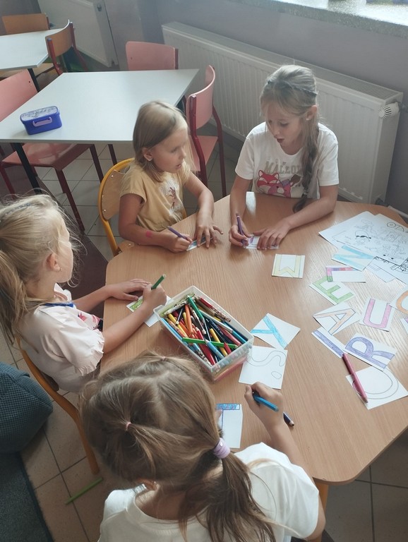 Dzieci kolorują literki na gazetkę świetlicową.